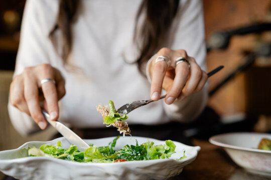 Close-up of Woman sitting at a table eating a fresh tuna salad with tomatoes and grated cheese