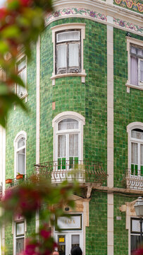 View of a traditional building facade with green azulejo tiles, white window frames, and an ornate balcony in Lagos, Faro District, Portugal.