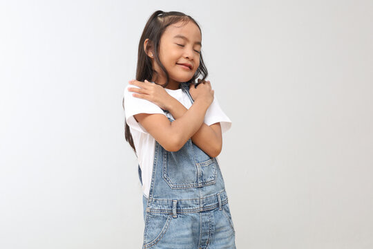 Happy and smiling Asian little girl hugging herself while closing her eyes, love yourself, be confident, feel proud, peaceful and relieved, mental health and self-respect concept