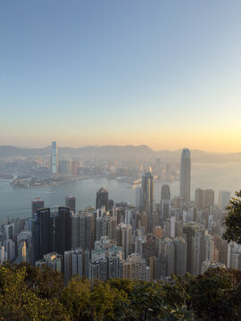 View of the dense urban skyline with skyscrapers, Victoria Harbour, and distant mountains during golden hour Hong Kong.