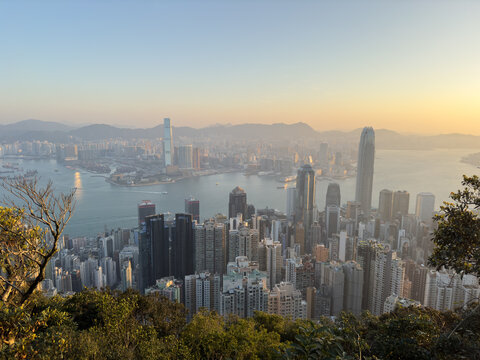 View of the dense urban skyline overlooking Victoria Harbour from Victoria Peak during golden hour with mountains in the background Hong Kong.