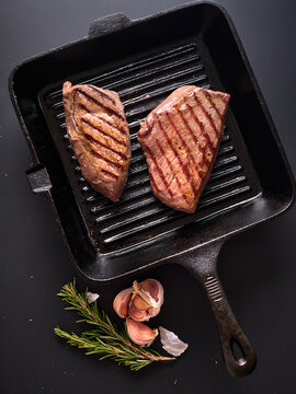 Grilled roast beef including flank and rump steak on a cast iron skillet on a black background with herbs and garlic