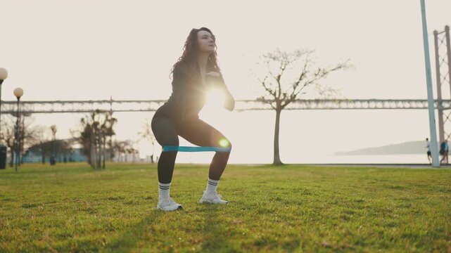 Athletic woman doing squats with resistance band outdoor