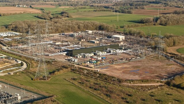 Aerial view of a sprawling substation complex amidst a patchwork of golden fields and verdant woodlands, Bramford, Ipswich, United Kingdom.