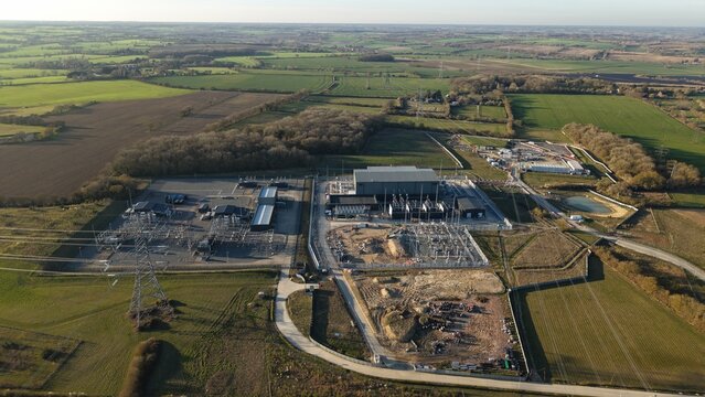 Aerial view of the Bramford Substation, a stark contrast of industrial grey against the patchwork green fields of Ipswich, United Kingdom.