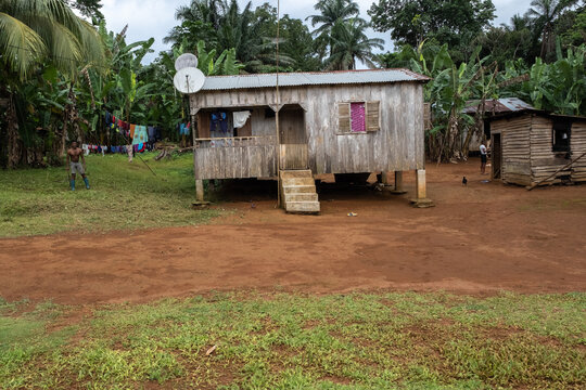 View of a traditional wooden stilt house with a satellite dish surrounded by lush tropical vegetation and palm trees in Sao Tome and Principe.