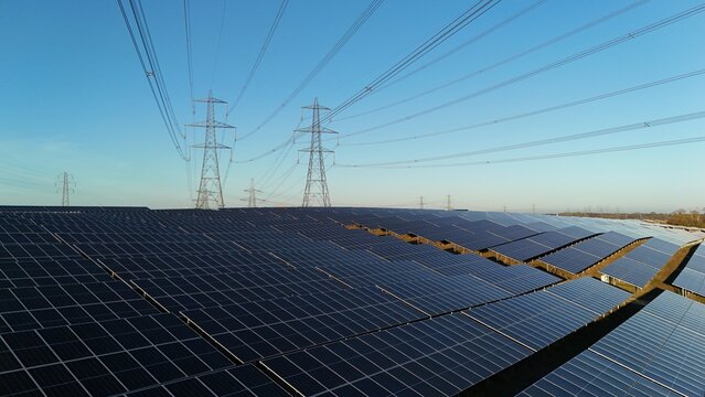 Aerial view of solar panels stretching out under the clear sky with electricity pylons, Tye Lane Solar farm, Ipswich, United Kingdom.