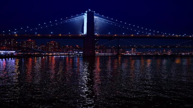 Sparkling river waterscape at night. Low angle view at the Brooklyn Bridge with illumination. New York, USA.