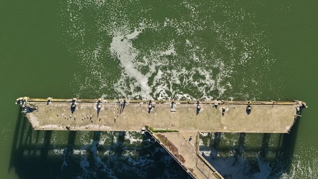 Aerial view of a concrete structure disappearing into dark green waters, as turbulent foam dances on the surface, Anglian Water Cliff Quay WRC, Ipswich, United Kingdom.