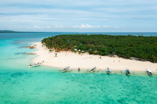 Aerial view of turquoise waters gently kissing the pristine white sands of the island, lush green vegetation contrasting against the bright sky, Virgin Island, Bantayan, Cebu, Philippines.