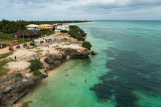 Aerial view of turquoise waters meeting the rugged coastline and sandy beach, near a cluster of buildings, Bantayan Island, Cebu, Philippines.