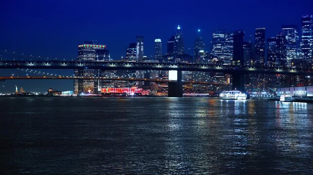 Moving over the surface of the river at night. Approaching the Manhattan Bridge and luminous skyline of New York in the backdrop.