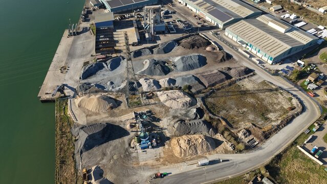 Aerial view of contrasting textures of gravel and sand piles sprawl across the industrial landscape where the river meets the port, Ipswich, United Kingdom.