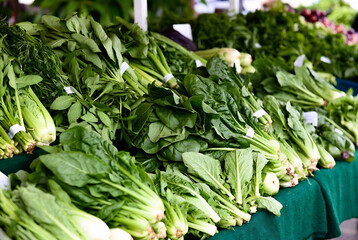 Obraz premium A display of fresh spinach and collard greens is at a farmer’s market. People are selling produce; the setting is an outdoor market.