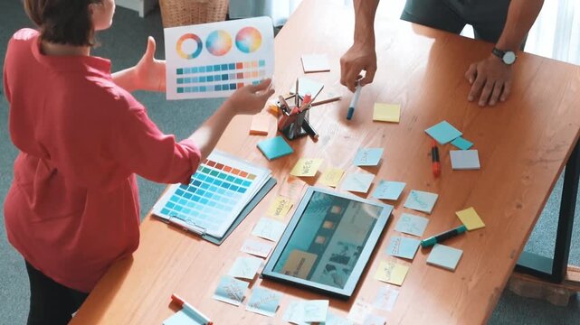 Top view of manager writing idea on sticky notes and explain idea about web design. Professional marketing team or programmer brainstorming idea while looking at tablet with color palette. Symposium.