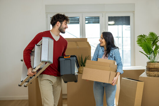 Young couple carrying a ladder and tool box while moving into their new home.