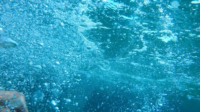 Dramatic underwater scene of male hand reaching toward the ocean surface with air bubbles and sunlight rays. Desperate hand struggling underwater to reach surface in deep ocean, 4K.