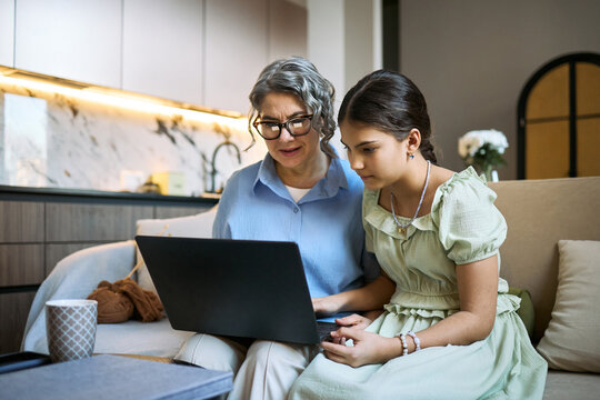 Middle aged woman and teenage girl using laptop together, reviewing online lesson or family finances at home. Suitable for education, digital literacy, parenting, remote support marketing