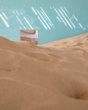 View of sand dunes filling an abandoned room with turquoise walls and sunlight patterns in Kolmanskop, Karas Region, Namibia.
