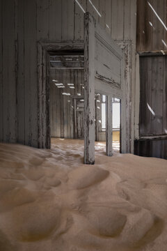 View of sand dunes filling the interior of an abandoned house with wooden doors and peeling paint in Kolmanskop, Karas Region, Namibia.