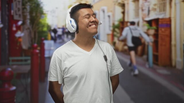 Man wearing white headset smiling with eyes closed, tilting head slightly and hands behind back on a street; joy music escape.