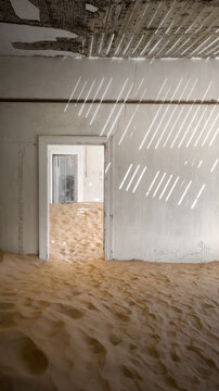 View of the interior of an abandoned house filled with desert sand dunes and sunlight patterns on the walls in Kolmanskop, Karas Region, Namibia.