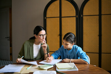 Middle aged woman tutoring teenage girl, reviewing homework and guiding writing at table. Useful for education support, homeschooling, mentoring, academic coaching campaigns