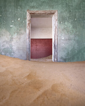 View of an abandoned room filled with desert sand dunes and peeling paint on the walls in Kolmanskop, Karas Region, Namibia.