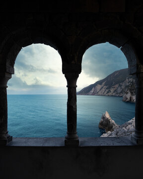 View of the blue sea and rocky cliffs through the stone arches of the Church of San Pietro, Porto Venere, Liguria, Italy.