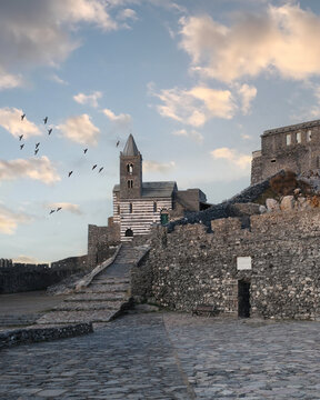 View of the historic Church of Saint Peter and ancient stone fortifications with birds flying in the sky at Porto Venere, Liguria, Italy.