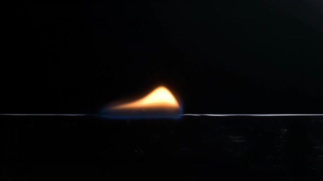 Closeup of a small bright orange and blue flame burning horizontally against a dark background