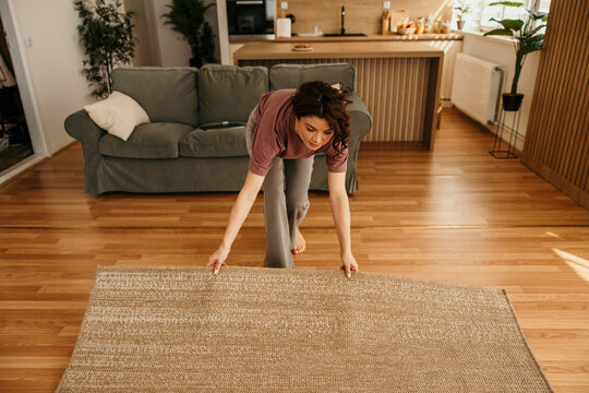 Woman unrolling rug on wooden floor in apartment