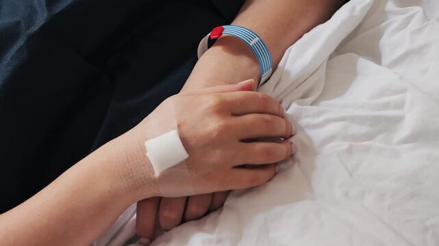 Recovering a patient who lies asleep in a hospital bed after surgery , hands on a blanket with information from the wristband. High quality 4k footage
