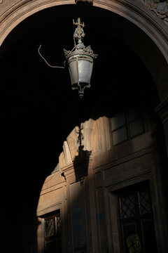 View of an ornate vintage street lamp hanging from a dark stone archway with historic architectural details and deep shadows Catania, Sicily, Italy.