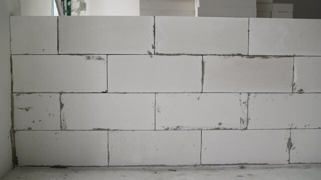 A worker lays a concrete block along a red laser level line during construction.