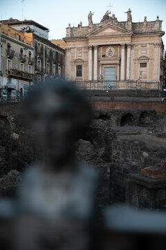 View of the ancient Roman Theatre ruins with the historic Church of San Biagio in the background under a clear sky in Catania, Sicily, Italy.