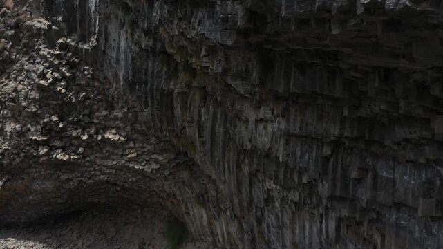 Aerial drone footage flying through a deep, scenic mountain gorge, revealing stunning, towering basalt column rock formations