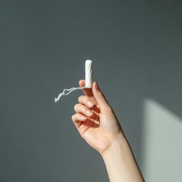 A hand holding a tampon applicator with a string attached