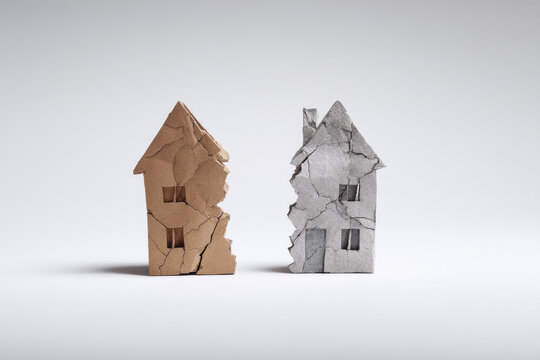 Two cracked models of cardboard houses on a light background.