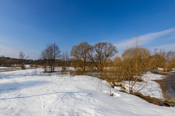 Obraz premium Snowy field beside river under clear blue sky