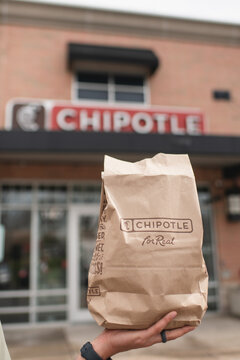 Aurora, IL/USA - March 26, 2026: Vertical close up photo of anonymous person's hand holding a Chipotle bag with Chipotle logo on it and the Chipotle sign is in background