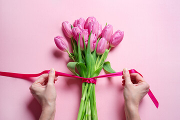 Woman hands tying pink ribbon on tulips, Mother's Day