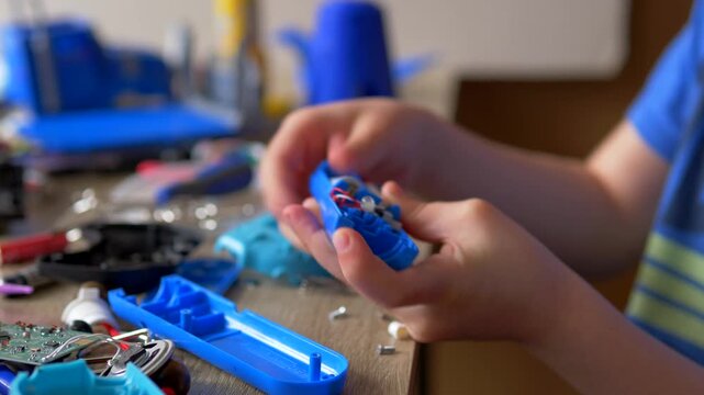 Child's Hands Inserting Batteries and Assembling Internal Parts of Blue Electronic Toy, Junior Technician Rebuilding a Circuit, Hands-on STEM Education and Repair Hobby