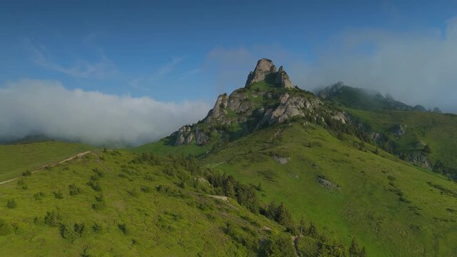 Majestic Ciucas Mountains orbital aerial view with unique wave-like orographic clouds rolling over spectacular rock peaks in Romania Carpathians, early summer sunrise