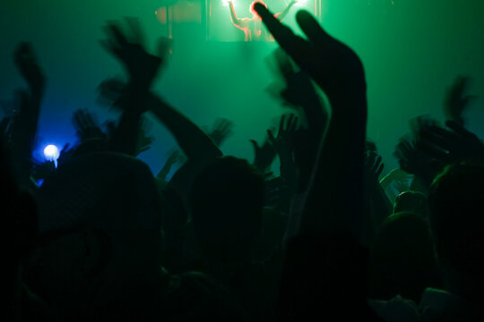 Silhouetted Crowd at Concert with Raised Hands and Stage Lighting