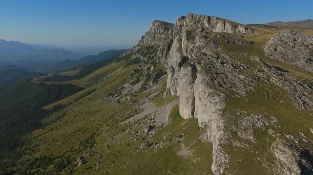 Spectacular rocky peaks of Coltii Tapului and Batrana on a steep mountain ridge under a clear blue sky at golden hour in the Bucegi Mountains, high altitude aerial orbit left