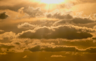 Barwne, złoto-pomarańczowe, zachmurzone niebo podczas epickiego zachodu słońca. Słońce jest częściowo zasłonięte, rzucając ciepłą poświatę na formacje chmur. Promienie światła rozchodzą się od słońca. © Grzegorz