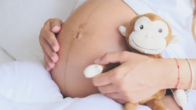 Expectant mother holding a monkey plush toy while tenderly rubbing her pregnant abdomen