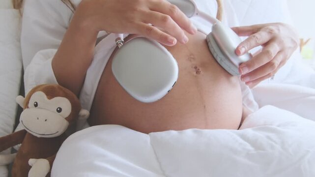 Expectant mother holding headphones on her pregnant belly for her unborn baby to listen to music