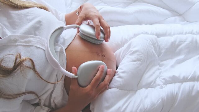 Expectant mother lying in bed placing headphones on her belly to play music for her unborn baby